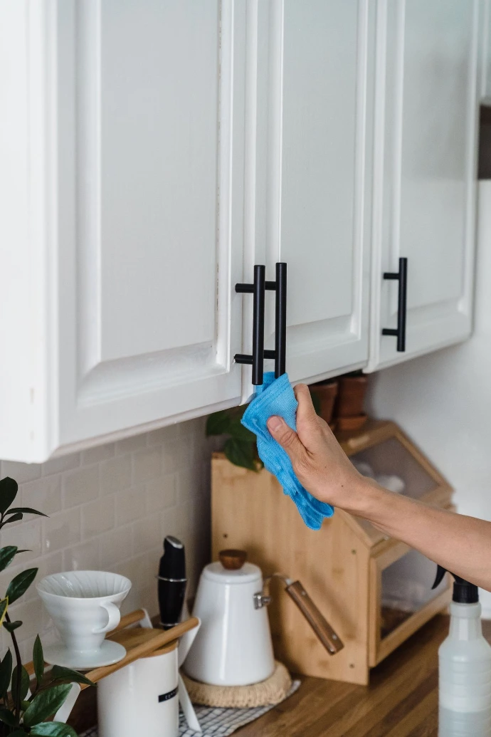 A person cleaning a white kitchen cabinet door 